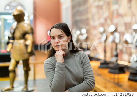 Interested woman viewing collection of medieval armor in museum 114251026