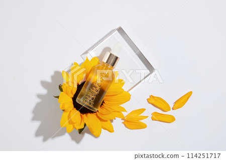 Blank label serum bottle with yellow liquid inside placed on sunflower above the transparent podium over white background. Mock up for advertising with blank space for text 114251717