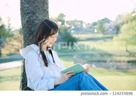 A woman reading a book under the cherry blossoms 114253696