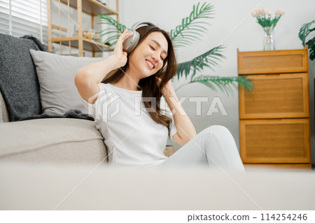 Joyful woman with closed eyes feeling the music through her headphones, sitting on a couch at home. Joyful woman with closed eyes feeling the music through her headphones, sitting on a couch at home. 114254246