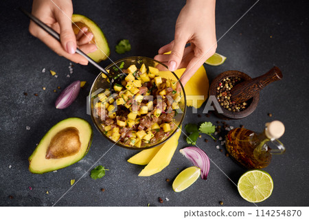 Woman mixing chopped tuna, mango, cilantro and onion in a glass bowl cooking traditional tuna and mango tartare 114254870