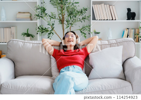 Relaxed young Asian woman enjoying rest on comfortable sofa 114254923