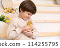 A boy sits at kitchen of rustic style and hugs little yellow duckling 114255795