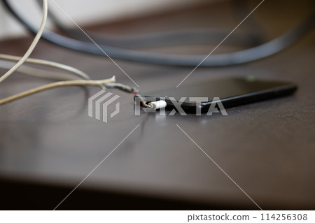 The smartphone is charging from a faulty cable. The concept of danger, the use of non-standard equipment, worn-out equipment 114256308