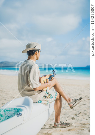 一名年輕人在夏威夷的沙灘上彈奏尤克里裡琴，背景是碧綠的海洋 114256807