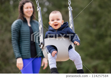 Caucasian Baby Boy on a swing with mother. Park Outside. 114257584