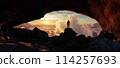 Adventure Man Standing in a Cave. Mountain Landscape in Background. Dramatic Sunset. 114257693