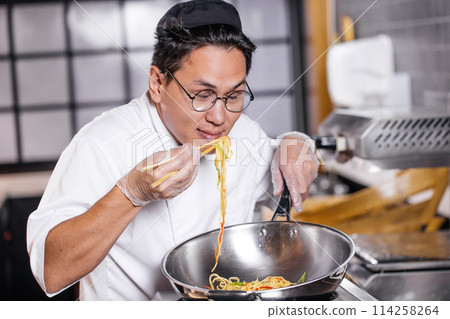 attractive Asian chef enjoying eating noodle attractive Asian chef enjoying eating noodle 114258264
