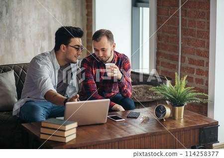 European gay male couple spend time together drinking coffee and watching laptop 114258377