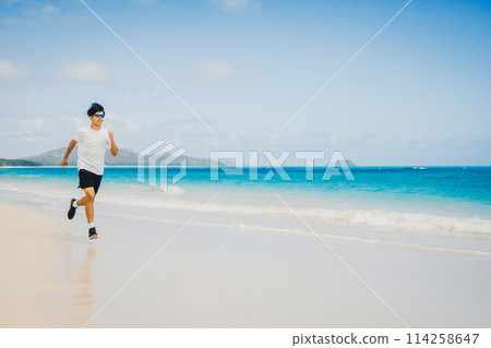 Young man running along the turquoise waters of a sandy Hawaii beach Young man running along the turquoise waters of a sandy Hawaii beach 114258647