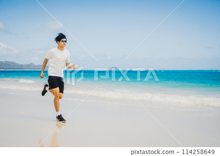 Young man running along the turquoise waters of a sandy Hawaii beach Young man running along the turquoise waters of a sandy Hawaii beach 114258649