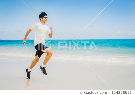 Young man running along the turquoise waters of a sandy Hawaii beach Young man running along the turquoise waters of a sandy Hawaii beach 114258651