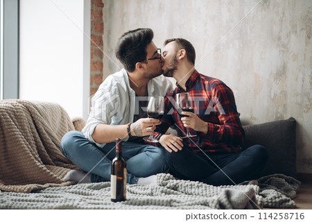 Laughing male gay couple drinking wine and preparing a meal Laughing male gay couple drinking wine and preparing a meal 114258716