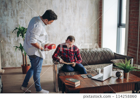 Happy surprised young handsome gay couple celebrating and giving gift at home 114258860