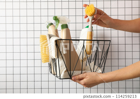 Basket with bottles of detergents and brushes in hands on light background Basket with bottles of detergents and brushes in hands on light background 114259213