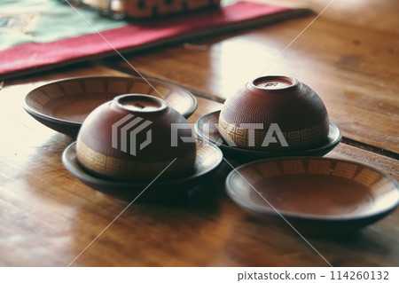 Close up view of a set of handmade brown earthen cups with simple ethnic design for tea or coffee resting on a wooden table, exuding cozy rustic charm and inviting warmth 114260132