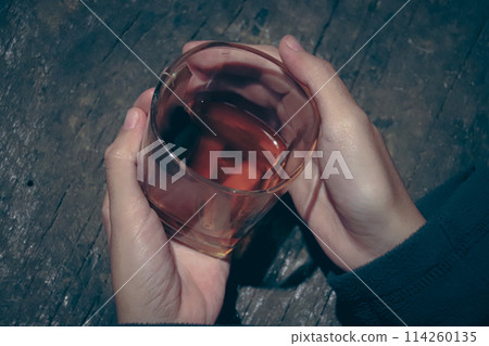 A close-up of a hand holding a glass with oolong or dark dragon black tea on a rustic wooden surface showing holistic healing and alternative medicine 114260135