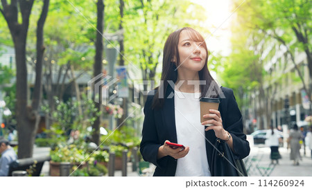 一位女商人帶著智慧型手機在城市裡行走 一位女商人帶著智慧型手機在城市裡行走 114260924