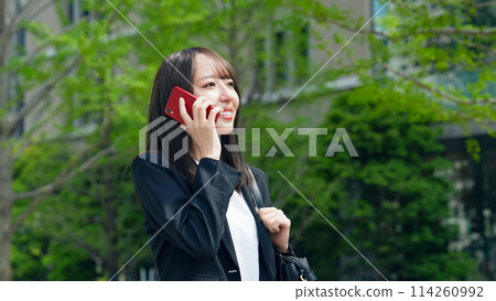 一位女商人在綠色城市中行走時用智慧型手機交談 114260992