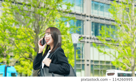 一位女商人在綠色城市中行走時用智慧型手機交談 114260995