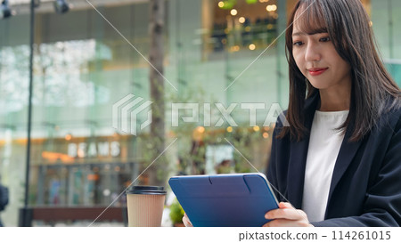 A woman looking at a tablet on a cafe terrace A woman looking at a tablet on a cafe terrace 114261015