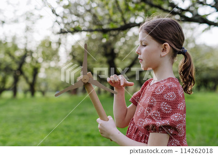 Girl standing outdoors in park, holding wind turbine. Renewable wind energy and sustainable lifestyle. 114262018