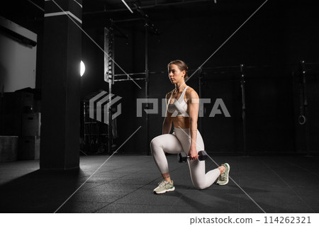 Woman performing dumbbell lunge, holding dumbells in both hands. Strength exercise. Routine workout for physical and mental health. 114262321