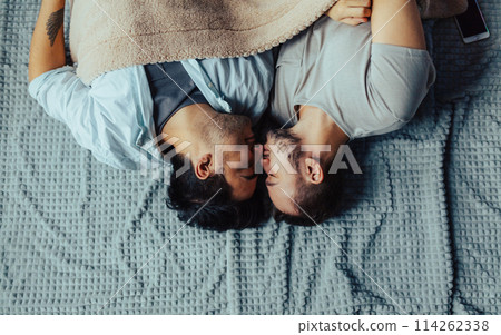 Handsome sleepy man with bristle kissing good night male partner lying in bed Handsome sleepy man with bristle kissing good night male partner lying in bed 114262338