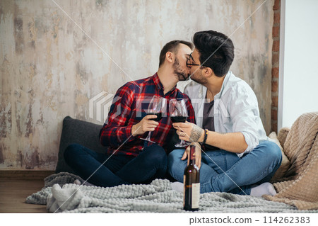 Laughing male gay couple drinking wine and preparing a meal Laughing male gay couple drinking wine and preparing a meal 114262383