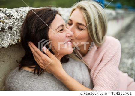 Adult daughter spending time with her mother outdoors. Beautiful daughter holding mother's face, kissing her cheek. Unconditional, deep maternal love, Mother's Day. 114262701