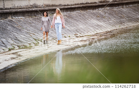 Adult daughter spending time with her mother. Mom and daughter outdoors, on walk by reservoir, lake embankment. Unconditional, deep maternal love, Mother's Day concept.. Adult daughter spending time with her mother. Mom and daughter outdoors, on walk by reservoir, lake embankment. Unconditional, deep maternal love, Mother's Day concept.. 114262718