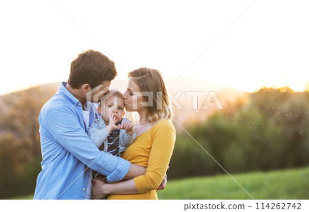 New parents holding small toddler, baby, outdoors in spring nature. Happy family moment New parents holding small toddler, baby, outdoors in spring nature. Happy family moment 114262742