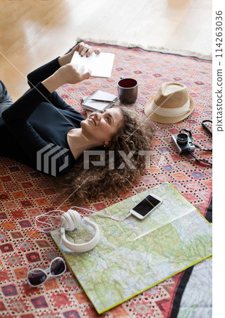 Woman planning summer vacation abroad, going on trip alone. Lying on carpet, daydreaming about adventures. Woman planning summer vacation abroad, going on trip alone. Lying on carpet, daydreaming about adventures. 114263036