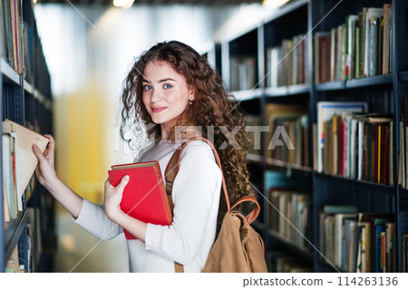Young female student in library, looking for books, preparing for final exam. 114263136