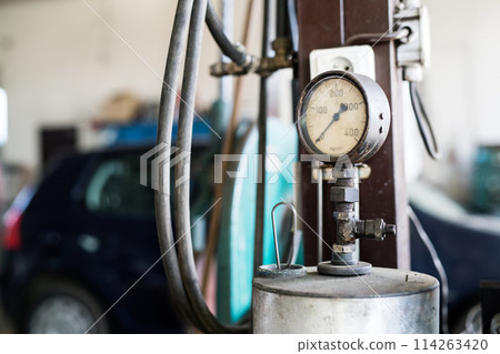 Tire-pressure gauge in auto repair shop. Mechanics repairing, maintaining car in garage, inspecting car tires, wheels. 114263420