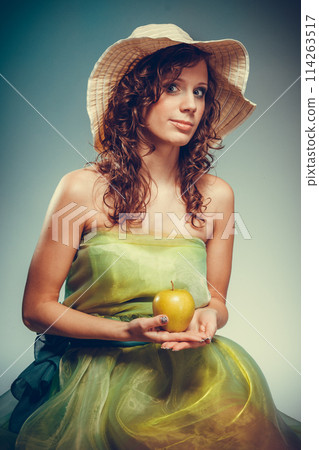 Woman in dress and hat holding yellow apple. Woman in dress and hat holding yellow apple. 114263517