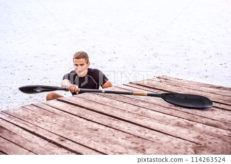 Canoeist man sitting in canoe holding paddle, getting out of water. Concept of canoeing as dynamic and adventurous sport. 114263524