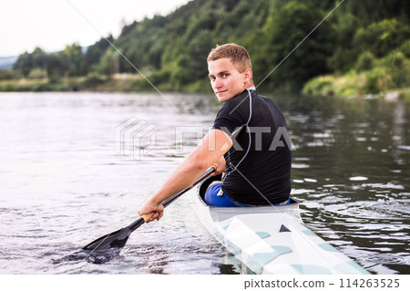 Canoeist man sitting in canoe holding paddle, in water. Concept of canoeing as dynamic and adventurous sport. Rear view, sportman looking at water surface, paddling 114263525
