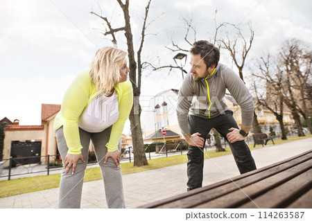 An overweight woman running in city with friend. Exercising outdoors for people with obesity, support from friend, fitness coach. An overweight woman running in city with friend. Exercising outdoors for people with obesity, support from friend, fitness coach. 114263587