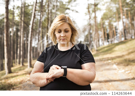 Overweight woman preparing for run in nature. Exercising outdoors for people with obesity. Overweight woman preparing for run in nature. Exercising outdoors for people with obesity. 114263644
