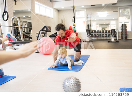 Father smiling at baby while performing exercise above. Group exercise class, fitness or pilates for parents. Parents staying active while boding with babies. 114263769