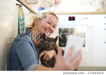 Beautiful mature woman at home, petting her cat. Older woman living alone, enjoying peaceful weekend day 114263818