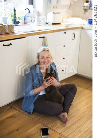 Beautiful mature woman at home, petting her cat. Older woman living alone, enjoying peaceful weekend day 114263823