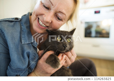 Beautiful mature woman at home, petting her cat. Older woman living alone, enjoying peaceful weekend day Beautiful mature woman at home, petting her cat. Older woman living alone, enjoying peaceful weekend day 114263825