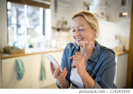 Beautiful mature woman at home, texting with friends. Older woman living alone, enjoying peaceful weekend day 114263830