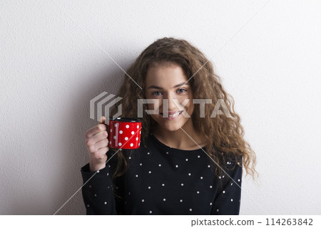 Portrait of a gorgeous teenage girl with curly hair drinking tea from mug. Studio shot, white background with copy space Portrait of a gorgeous teenage girl with curly hair drinking tea from mug. Studio shot, white background with copy space 114263842