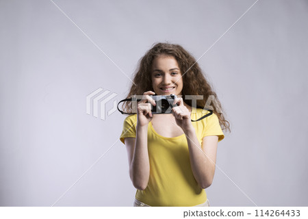 Portrait of a gorgeous teenage girl with curly hair holding camera. Studio shot, white background with copy space Portrait of a gorgeous teenage girl with curly hair holding camera. Studio shot, white background with copy space 114264433