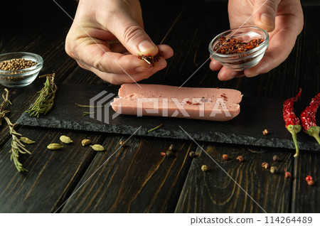 Chef prepares aromatic sausage with spices on the kitchen table. The cook hand adding dry seasoning to raw sausage before baking. Free space for advertising 114264489