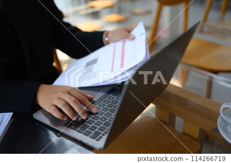 Finance Investment analyst holding documents and using laptop at office desk Finance Investment analyst holding documents and using laptop at office desk 114266719