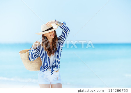 happy elegant woman on seashore with straw bag 114266763